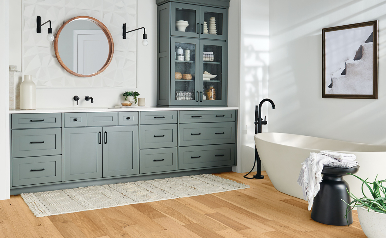 natural hardwood flooring in bathroom with gray-blue vanity and white soaker tub